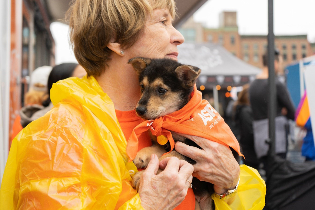 A woman holding a puppy wearing an orange bandana