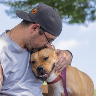 A man kissing a brown dog on the head