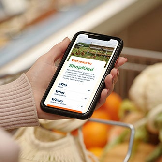 Person holding smartphone with ASPCA ShopKind website on screen above shopping cart