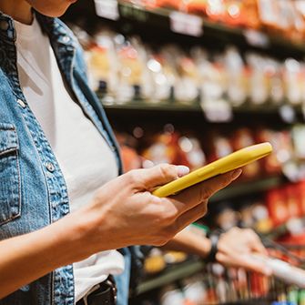 Close up on a woman's hand holding a phone in yellow case while standing a grocery store aisle