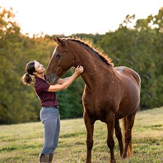 a woman with a horse outside with trees in the background