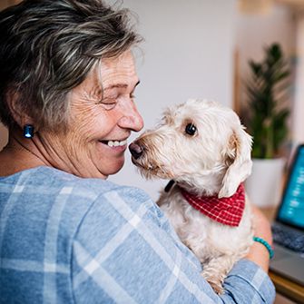 an elderly woman holding a small white dog in front of her laptop