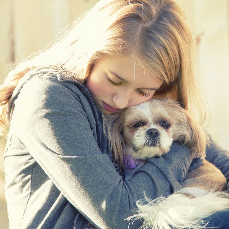 a blonde girl in a grey hoodie hugging a small dog