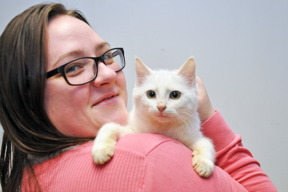 Woman wearing a pink sweater holding small white cat